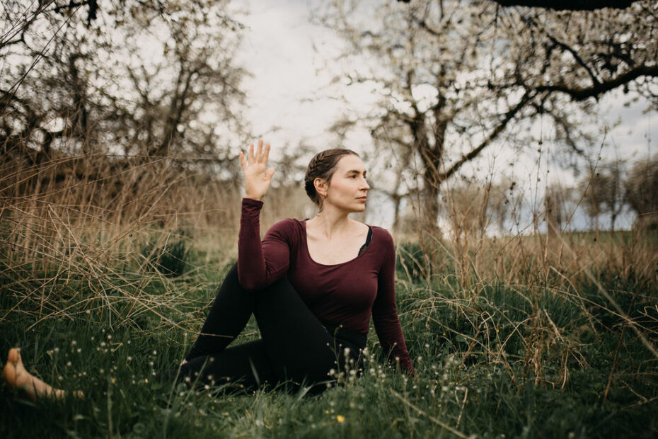 Yogalehrerin sitzt meditierend in der Natur bei Sonnenaufgang, umgeben von Erdelementen – symbolisiert die Verbindung von Ayurveda und Yoga für Körper und Geist.