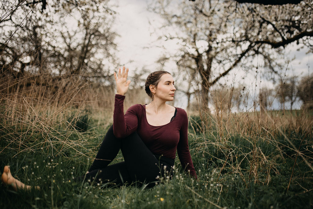 Yogalehrerin sitzt meditierend in der Natur bei Sonnenaufgang, umgeben von Erdelementen – symbolisiert die Verbindung von Ayurveda und Yoga für Körper und Geist.